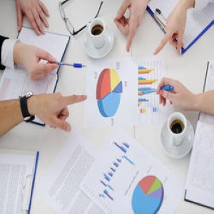 Peoples fingers pointing to a variety of graphs on a desk in a meeting.